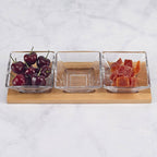 Three glass bowls on a wooden stand with cherries, a clear item, and dried fruits against a light background