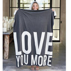 dark gray blanket with 'LOVE YOU MORE' text in a modern indoor setting.