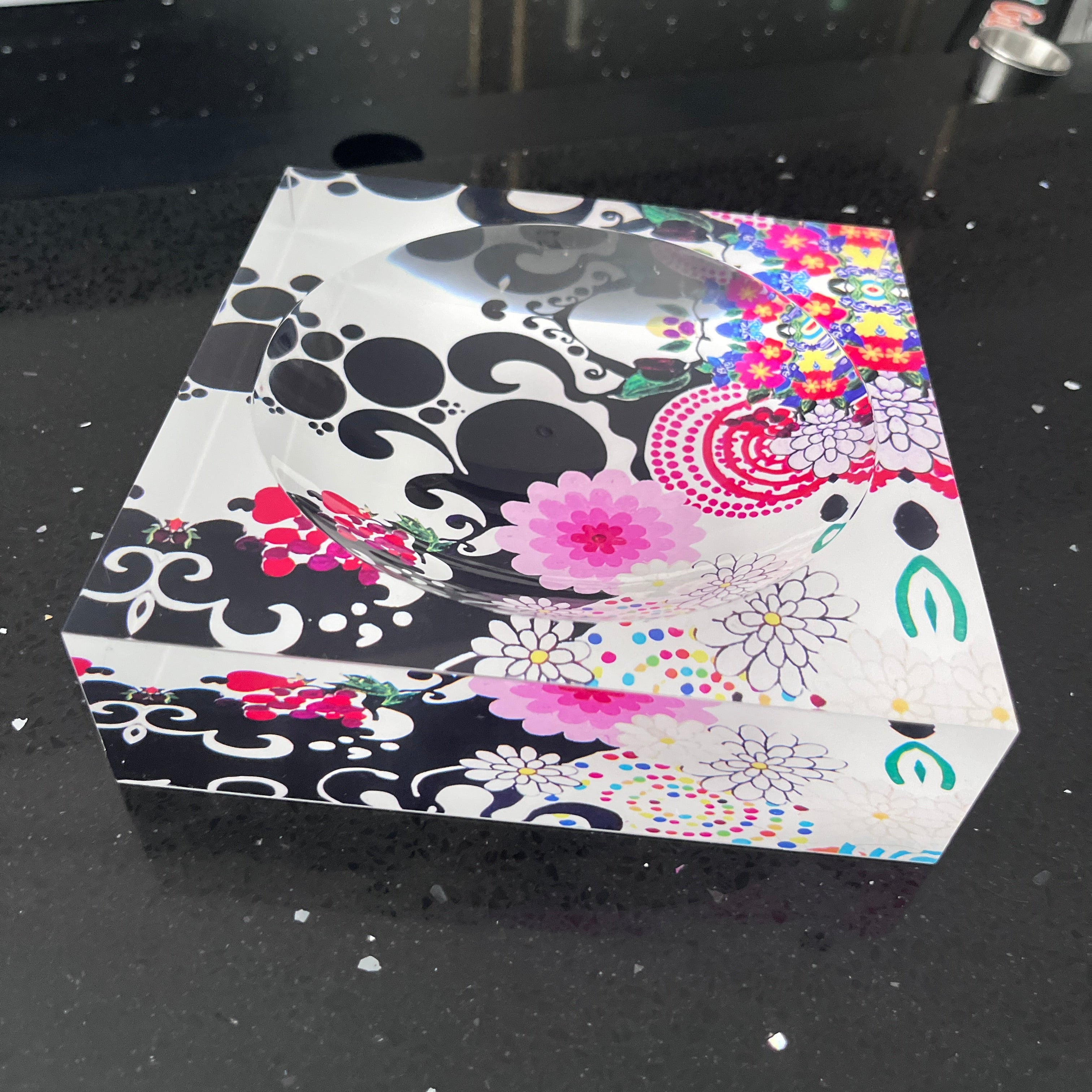 Decorative acrylic candy dish with floral and abstract patterns on a black background