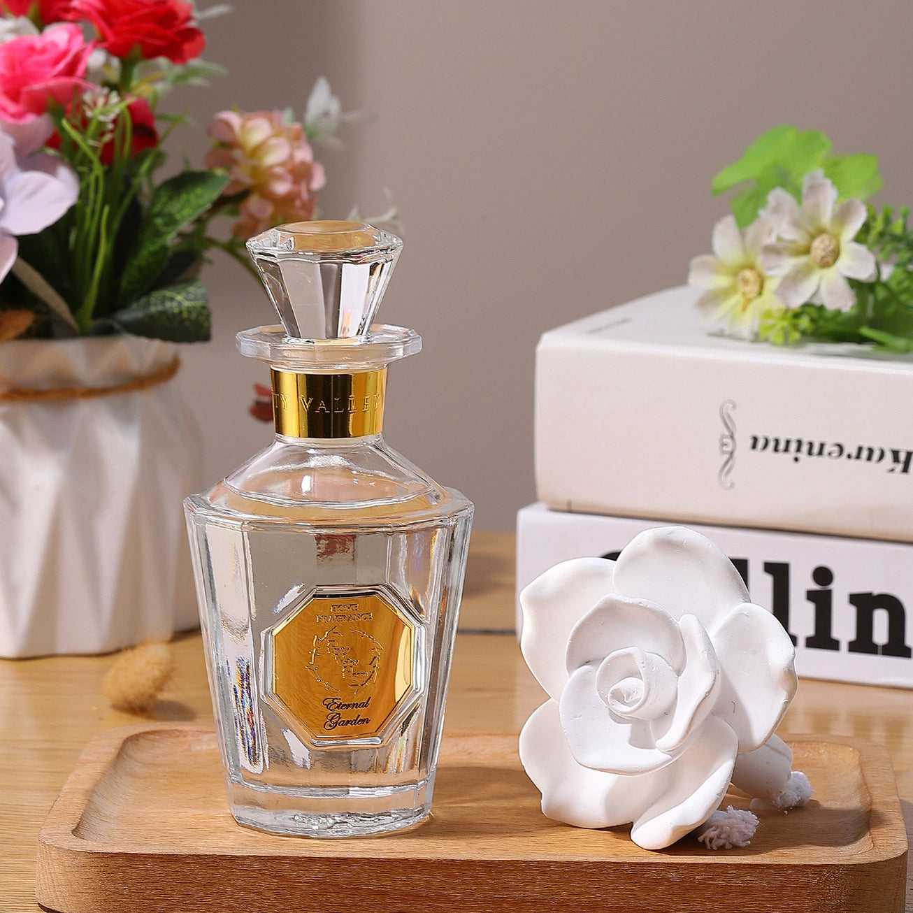 Glass perfume bottle with gold cap on a wooden tray with flowers and books in the background