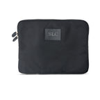 A black laptop sleeve with a monogrammed label on the front, featuring a zipper closure.