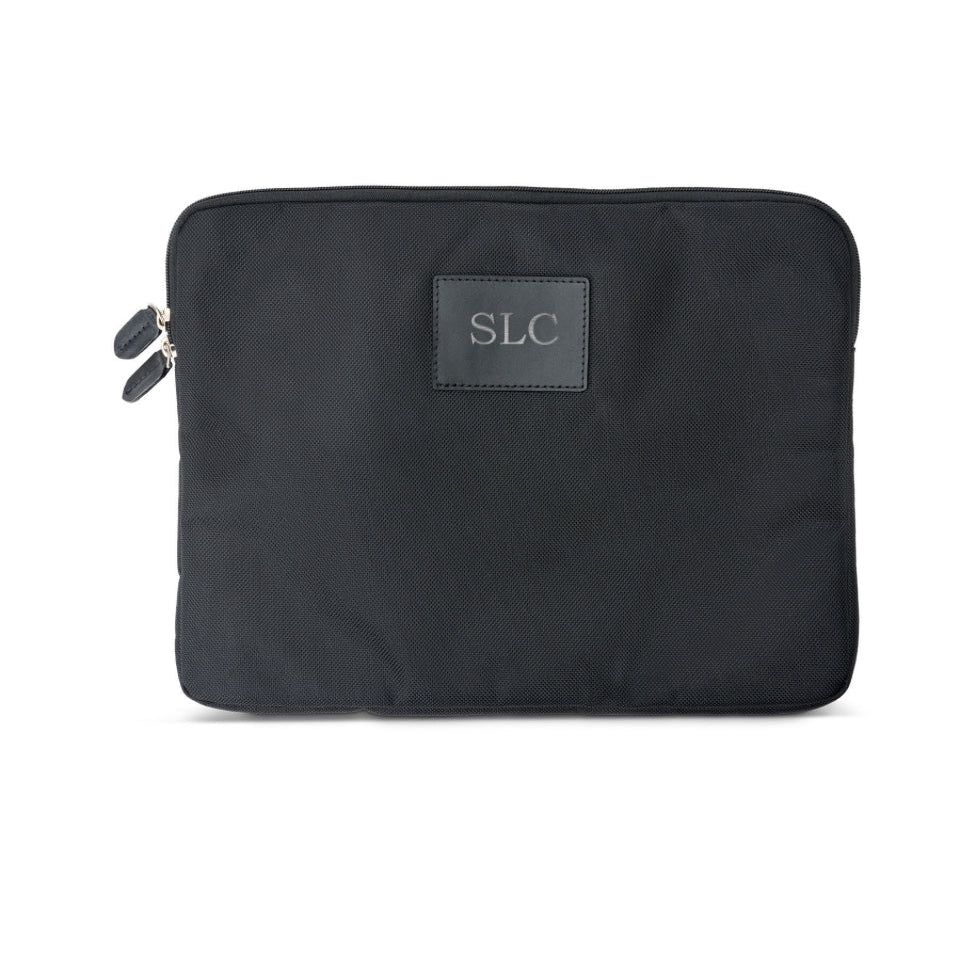 A black laptop sleeve with a monogrammed label on the front, featuring a zipper closure.