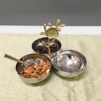 Three metal bowls with a decorative sun-like object on a textured surface with red flowers.
