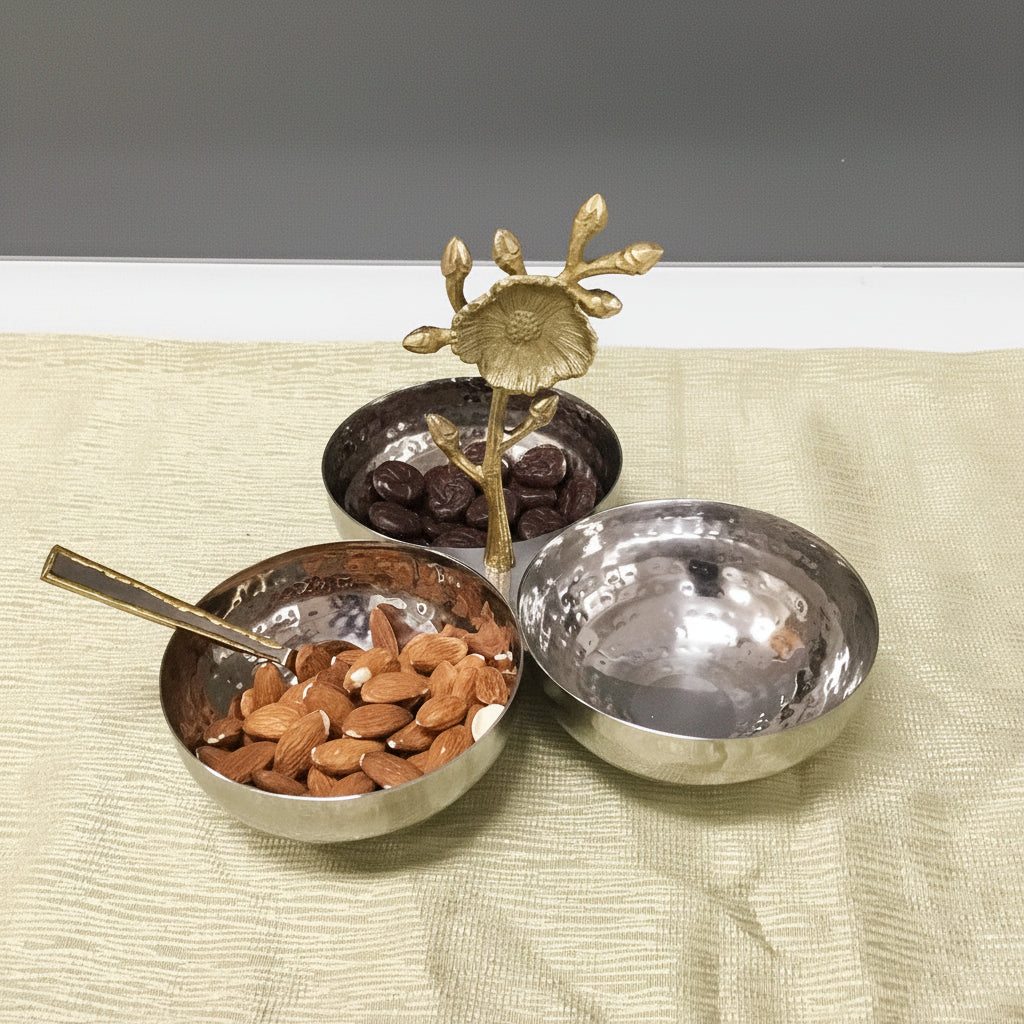 Three metal bowls with a decorative sun-like object on a textured surface with red flowers.